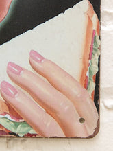 Load image into Gallery viewer, A close-up of a vintage-style illustrated sign or print showing a hand with pink manicured nails resting on a sandwich slice, with a small hole near the lower right edge.
