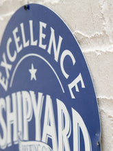 Load image into Gallery viewer, A close-up of a blue oval sign with white lettering reading 'EXCELLENCE SHIPYARD' mounted against a light textured wall.

