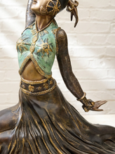 Load image into Gallery viewer, A close-up of a decorative figurine or sculpture of a woman in flowing dark bronze clothing with a turquoise-green bodice and gold detailing, shown against a light brick wall background.
