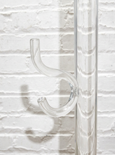 Load image into Gallery viewer, Vintage freestanding clear Lucite coat rack featuring a tall transparent cylindrical column, curved transparent hooks at different heights, and a round clear base.
