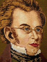 Load image into Gallery viewer, Close-up of a needlepoint or embroidered portrait showing part of a person's face with brown hair, round glasses, red lips, a white ruffled collar, and a dark patterned neckwear against an olive-brown textured background.
