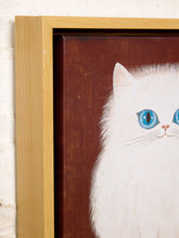 Load image into Gallery viewer, A close-up of a framed painting featuring a white cat with bright blue eyes on a dark brown background, set in a light wood frame against a white brick wall.
