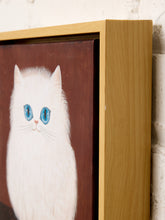Load image into Gallery viewer, A close-up of a framed painting featuring a fluffy white cat with bright blue eyes on a dark brown background, set in a light wood frame against a white brick wall.

