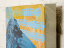 Load image into Gallery viewer, A close-up of a textured canvas painting showing a blue bird against a yellow and light blue patterned background, with the side of the canvas wrapped in beige tape against a white brick wall.
