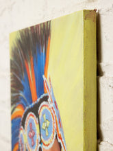 Load image into Gallery viewer, A close-up of a colorful canvas painting showing part of a feathered headdress with blue, orange, red, and black feathers against a pale yellow background, mounted on a white brick wall.
