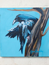 Load image into Gallery viewer, A square canvas painting of a black and white raven perched on a brown tree trunk against a bright blue background, mounted on a white brick wall. The artist's signature 'Glen Bradley' is visible in the bottom right corner.
