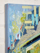 Load image into Gallery viewer, Abstract canvas wall art hanging on a white brick wall, featuring layered brushstrokes and splatters in blue, navy, yellow, green, white, and red.
