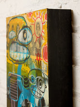 Load image into Gallery viewer, A square black wooden canvas print featuring a colorful graffiti-style cartoon face design, leaning against a white brick wall.
