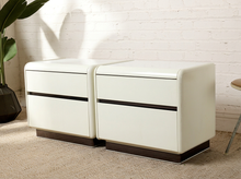 Load image into Gallery viewer, Pair of vintage postmodern white nightstands featuring glossy rectangular bodies, softly rounded corners, two handleless drawers each, and smoked translucent plinth bases.
