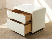 Load image into Gallery viewer, A modern two-drawer nightstand with a glossy white finish and light wood interiors, shown open on a carpeted floor against a white brick wall.
