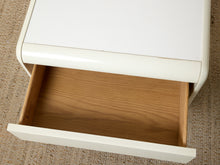 Load image into Gallery viewer, A close-up of a white drawer-front furniture piece with one drawer pulled open, showing a light wood interior, set on a beige textured rug.
