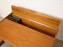Load image into Gallery viewer, Image 15 of 22: A mid-century modern wooden desk with a lift-top storage compartment, shown open against a white brick wall.
