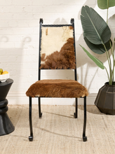 Load image into Gallery viewer, Image 1 of 15: Vintage accent chair featuring a brown cowhide upholstered seat, rectangular backrest with natural brown and cream cowhide pattern, black wrought iron frame, decorative scrollwork at the top, and curved metal legs.

