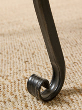 Load image into Gallery viewer, Image 15 of 15: Close-up of a dark metal chair leg with a curved hook base resting on a beige woven burlap surface.
