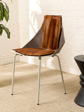 Load image into Gallery viewer, Image 2 of 16: A mid-century modern accent chair with a brown leather seat and backrest, supported by a slim silver metal frame, set in a room with a white brick wall and beige carpet.
