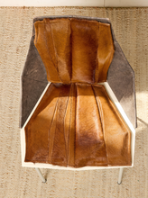 Load image into Gallery viewer, Image 4 of 16: A modern sculptural chair with a pleated brown leather seat and backrest, dark gray side panels, and a white geometric frame, set on a woven jute rug.
