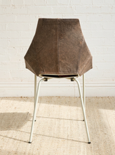 Load image into Gallery viewer, Image 6 of 16: A mid-century modern chair with a textured brown leather seat and a white metal frame, set against a white brick wall and a woven jute rug.
