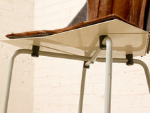 Load image into Gallery viewer, Image 14 of 16: Close-up of a mid-century modern chair featuring a cream-colored molded plastic seat shell, brown leather upholstery, and light gray tubular metal legs, set against a white brick wall background.

