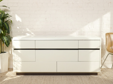 Load image into Gallery viewer, Image 1 of 18: Vintage postmodern white lacquer dresser featuring a long rectangular silhouette, softly rounded corners, asymmetrical geometric drawer fronts, recessed horizontal pulls, and a black plinth base.
