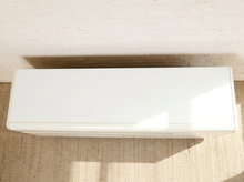 Load image into Gallery viewer, Image 4 of 18: Vintage postmodern white lacquer dresser featuring a long rectangular silhouette, softly rounded corners, asymmetrical geometric drawer fronts, recessed horizontal pulls, and a black plinth base.
