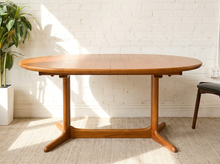 Load image into Gallery viewer, Image 2 of 28: Vintage Danish modern teak dining table featuring an oval golden-brown wood tabletop with visible natural grain, softly rounded edges, and a sculptural trestle base with angled feet. Includes two extension leaves.

