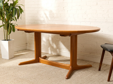 Load image into Gallery viewer, Image 3 of 28: Vintage Danish modern teak dining table featuring an oval golden-brown wood tabletop with visible natural grain, softly rounded edges, and a sculptural trestle base with angled feet. Includes two extension leaves.
