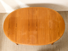 Load image into Gallery viewer, Image 4 of 28: An oval wooden table with a warm honey-toned finish and visible wood grain, photographed from above against a light textured floor and white wall.
