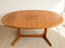 Load image into Gallery viewer, Image 5 of 28: An oval mid-century modern wooden dining table with a warm honey finish, set on a textured beige rug against a white brick wall.
