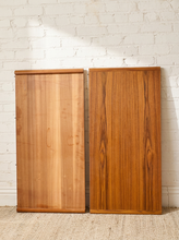 Load image into Gallery viewer, Image 15 of 28: Two rectangular wooden panels with vertical grain, one in a lighter honey tone and one in a richer medium brown, leaning against a white painted brick wall on a woven rug.
