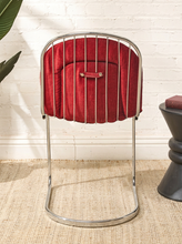 Load image into Gallery viewer, Image 8 of 15: A mid-century modern style chair with a curved chrome metal frame and a deep red velvet upholstered seat, set against a white brick wall and woven jute rug.
