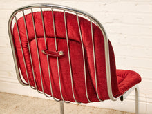 Load image into Gallery viewer, Image 12 of 15: A close-up of a mid-century modern chair featuring a red velvet upholstered backrest and seat cushion with a polished chrome tubular metal frame, set against a white brick wall background.
