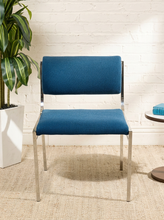 Load image into Gallery viewer, Image 2 of 14: Vintage dining chair featuring a navy blue upholstered seat, curved cylindrical padded backrest, open-back design, and slender chrome metal frame with angled legs.
