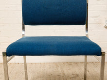 Load image into Gallery viewer, Image 10 of 14: A mid-century modern dining chair with a deep blue upholstered seat and backrest, supported by a chrome steel frame, set against a white brick wall.
