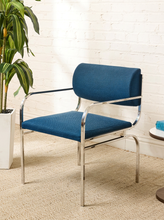 Load image into Gallery viewer, Image 1 of 15: Vintage dining armchair featuring a navy blue upholstered seat, curved cylindrical padded backrest, open-back design, polished chrome armrests, and slender angled metal legs.
