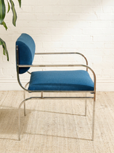 Load image into Gallery viewer, Image 4 of 15: Vintage dining armchair featuring a navy blue upholstered seat, curved cylindrical padded backrest, open-back design, polished chrome armrests, and slender angled metal legs.
