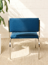 Load image into Gallery viewer, Image 5 of 15: Vintage dining armchair featuring a navy blue upholstered seat, curved cylindrical padded backrest, open-back design, polished chrome armrests, and slender angled metal legs.
