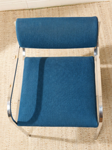 Load image into Gallery viewer, Image 6 of 15: Vintage dining armchair featuring a navy blue upholstered seat, curved cylindrical padded backrest, open-back design, polished chrome armrests, and slender angled metal legs.

