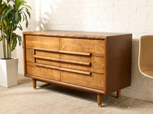 Load image into Gallery viewer, Image 2 of 16: Restored Guild of California mid-century modern six-drawer dresser featuring a warm honey-brown wood finish, three stacked drawers on each side, long sculptural horizontal wooden pulls, softly rounded cabinet edges, and short tapered legs.

