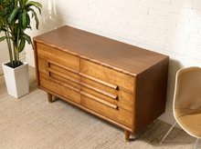 Load image into Gallery viewer, Image 3 of 16: Restored Guild of California mid-century modern six-drawer dresser featuring a warm honey-brown wood finish, three stacked drawers on each side, long sculptural horizontal wooden pulls, softly rounded cabinet edges, and short tapered legs.

