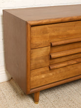 Load image into Gallery viewer, Image 5 of 16: Mid-century modern wooden dresser with three drawers, curved drawer pulls, and tapered legs, shown against a white brick wall and textured rug.
