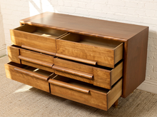 Load image into Gallery viewer, Image 14 of 16: Mid-century modern wooden dresser with six drawers, some open, featuring a warm medium-brown wood finish and curved drawer pulls, set against a white brick wall and carpeted floor.
