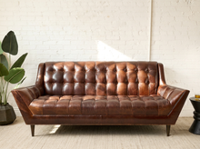 Load image into Gallery viewer, Image 1 of 13: Modern three-seater sofa featuring cognac brown leather upholstery, deep square button tufting across the backrest and seat, angular upholstered arms, and short tapered legs.
