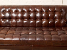Load image into Gallery viewer, Image 6 of 13: A close-up of a dark brown tufted leather sofa, showing the button-tufted backrest and seat cushion against a white brick wall background.
