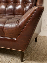 Load image into Gallery viewer, Image 9 of 13: Close-up of a dark brown leather tufted sofa arm and seat corner, showing the leather texture, dark wooden legs, and a woven jute rug.
