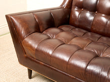 Load image into Gallery viewer, Image 10 of 13: Close-up of a dark brown tufted leather sofa corner with visible grain and a small dark leg, photographed indoors on a light carpet.
