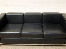 Load image into Gallery viewer, Image 6 of 14: A three-seat black leather sofa with a chrome metal frame, positioned against a white brick wall and a light-colored carpet.
