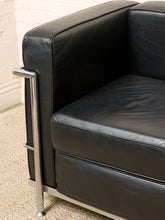 Load image into Gallery viewer, Image 7 of 14: Close-up of a black leather armchair with a polished chrome metal frame, showing the armrest, seat cushion, and leg on a carpeted floor.

