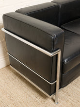 Load image into Gallery viewer, Image 8 of 14: Close-up of a black leather armchair with a polished chrome tubular steel frame, positioned on a textured beige carpet against a white brick wall.
