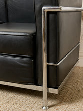 Load image into Gallery viewer, Image 10 of 14: Close-up of a black leather armchair with a polished chrome metal frame and leg, resting on a woven beige rug.
