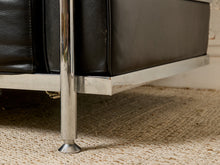 Load image into Gallery viewer, Image 14 of 14: Close-up detail of a black leather sofa with a polished chrome metal frame and leg, resting on a beige woven rug.
